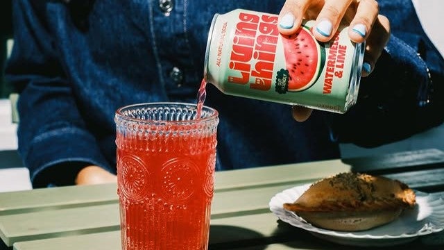 red soda drink being poured into glass by woman wearing denim jacket.