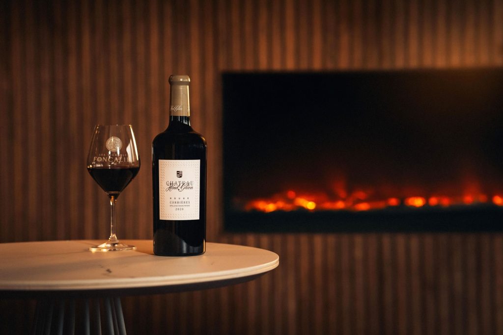 red wine bottle and glass on table inside by electric fire.
